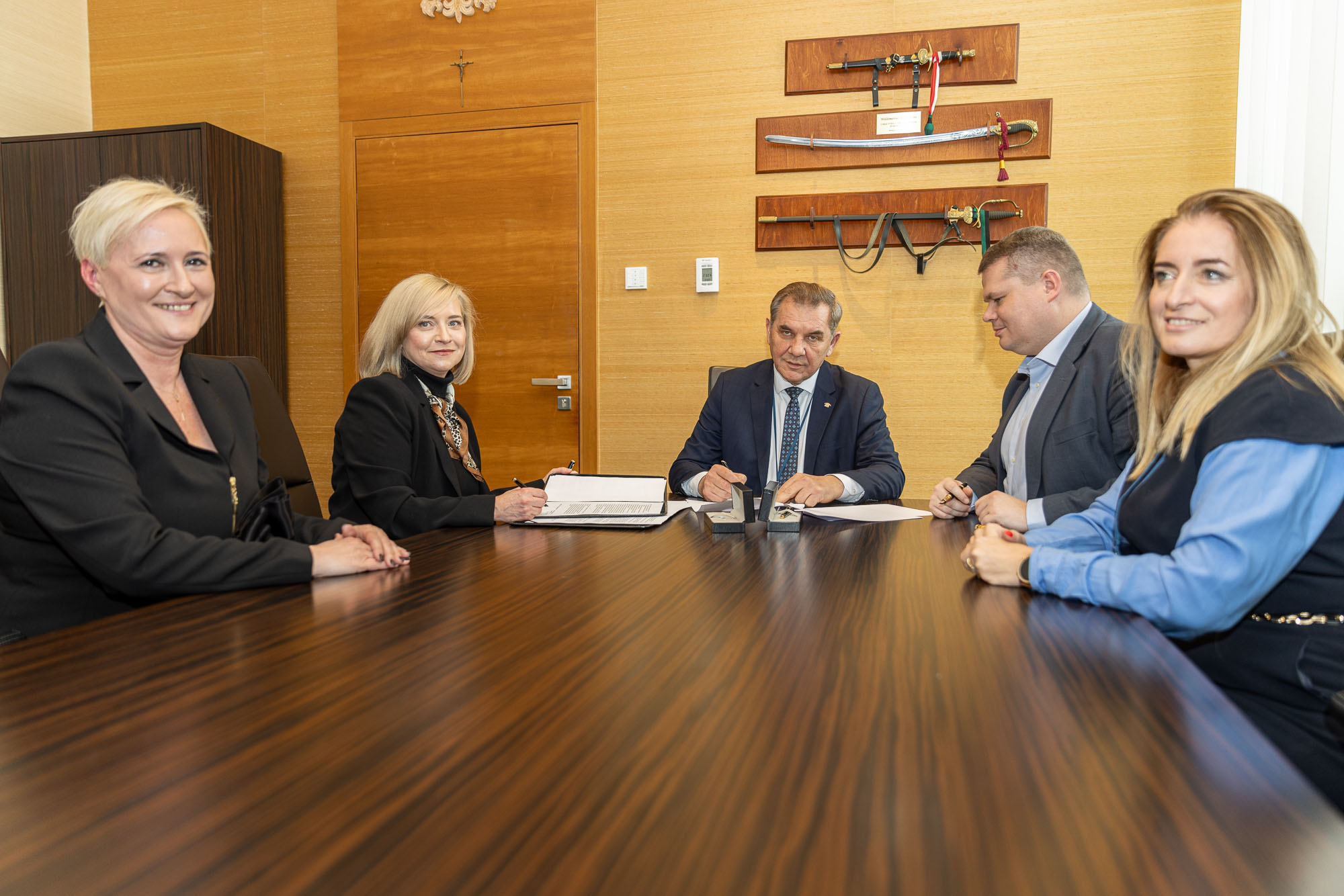 Three women and two men in elegant clothes sitting at a conference table
