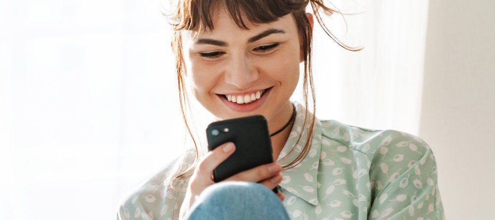 Zdjęcie uśmiechniętej dziewczyny czytającej na telefonie