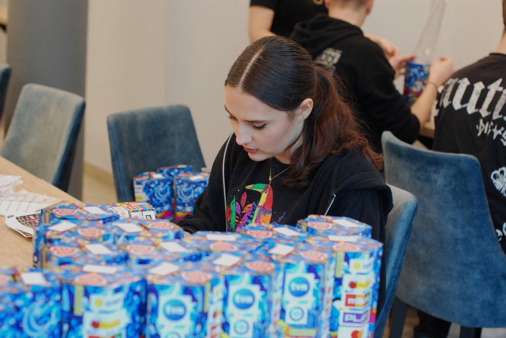 A student from the WOSP UniLodz Staff sitting at a table with collection boxes for the WOSP charity 