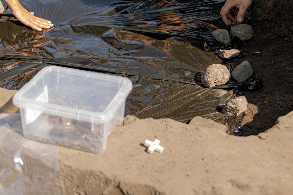 plastikowe pudełko z fragmentami kostnymi, w tle przykryta folią ziemia