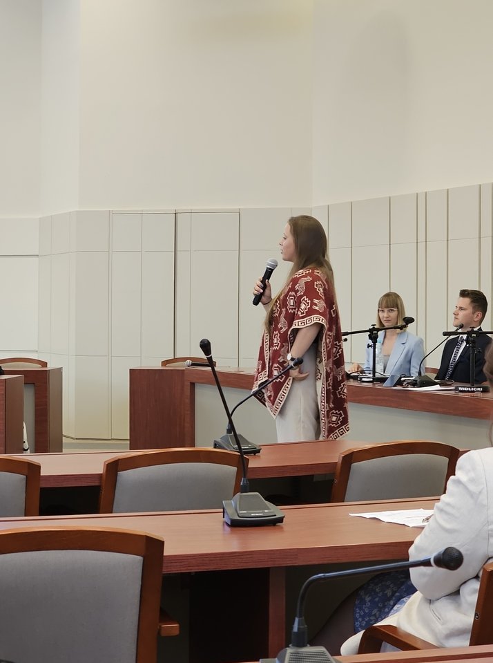 Karina Woźniak stoi z mikrofonem w sali wykładowej