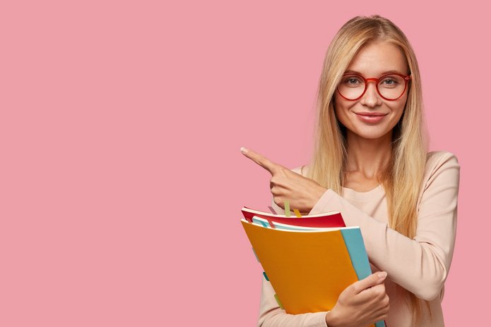 Zdjęcie-uśmiechnięta studentka trzyma trzy kolorowe zeszyty