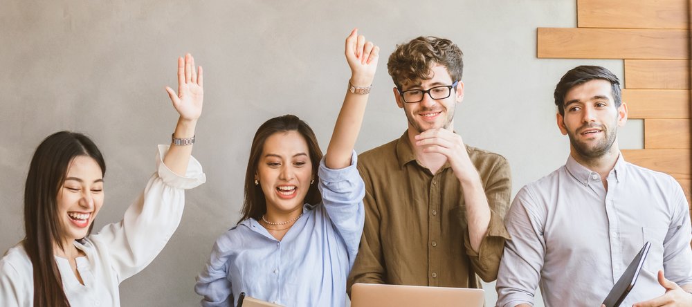 2 young women with their arms raised in a gesture of joy and 2 young smiling men
