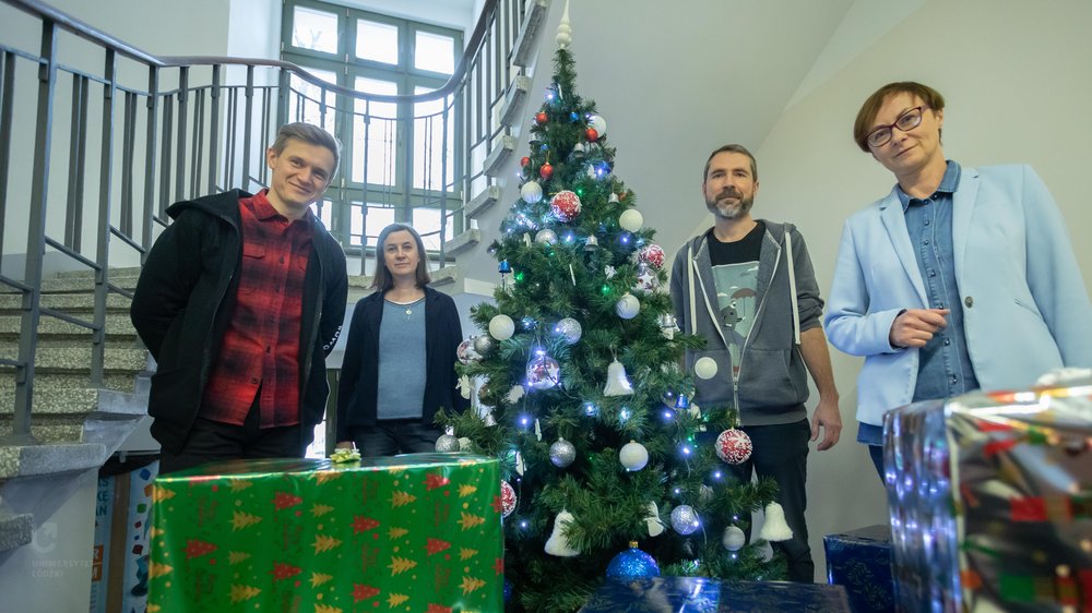 Four persons standing next to a Christmas tree and gifts 