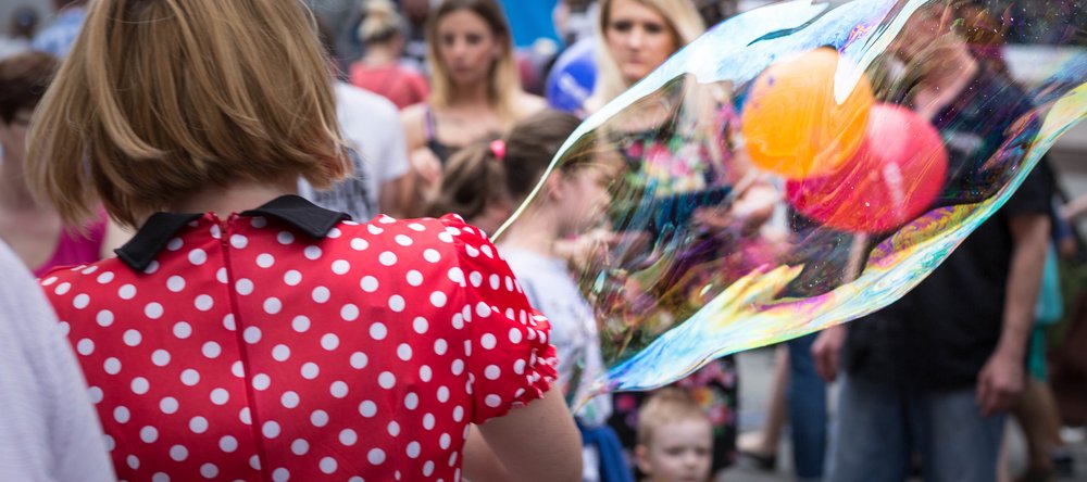 A woman wearing a red dress with white polka dots with soap bubbles, other people visible in the background