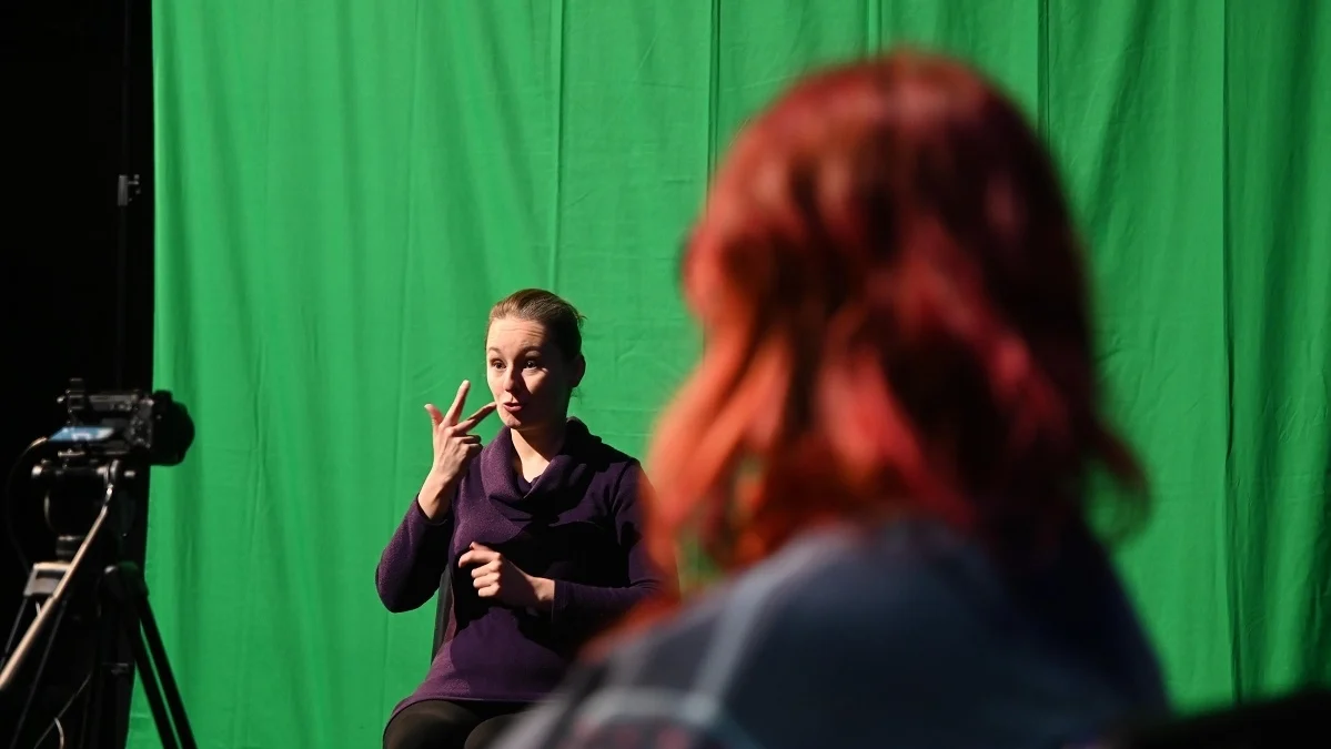 A photo showing a person using sign language and a person looking at a sign language interpreter